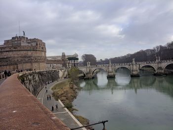 Arch bridge over river against cloudy sky