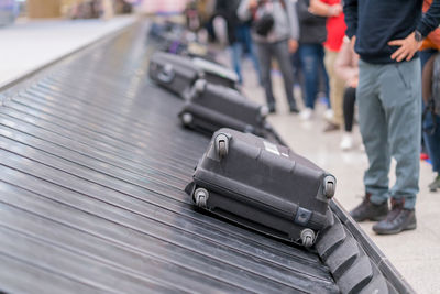 Low section of people standing by suitcases on conveyor belt at airport