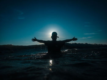 Silhouette man in sea against sky during sunset