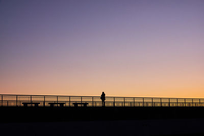 Silhouette man standing on bridge against clear sky during sunset
