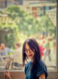 Young woman in eyeglasses sitting beside window and looking away.