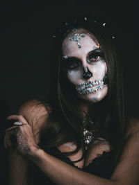 Close-up portrait of young woman with spooky face paint against black background