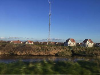 Houses by river and buildings against clear blue sky