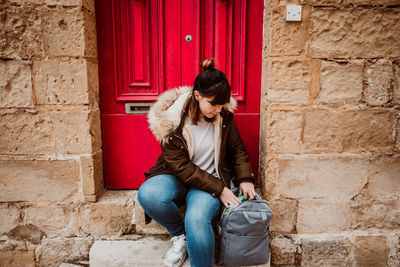 Full length of woman with backpack sitting by door