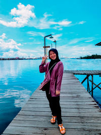 Full length portrait of woman standing on pier over lake against sky