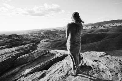 Rear view of woman standing on rock against sky