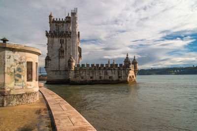 Belem tower in tagus river against cloudy sky