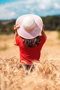 Rear view of woman wearing hat standing amidst wheat on field during sunny day