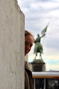 Portrait of woman standing wall against statue