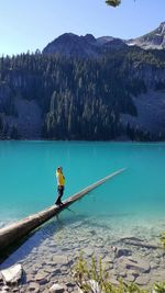 Full length of woman standing on fallen tree trunk in lake by mountain