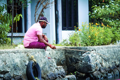 Side view of man sitting on retaining wall