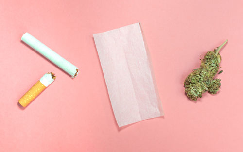 Materials to roll cannabis joint with tobacco on pink background.