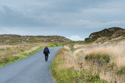 Rear view of man walking on road against sky