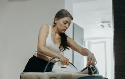 A young girl irons clothes at home.