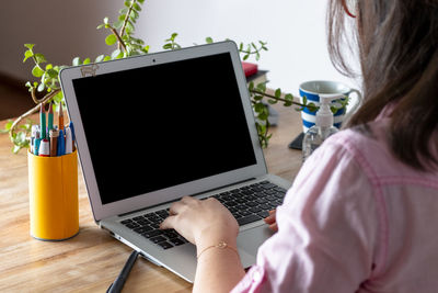 Rear view of woman using laptop on table at home