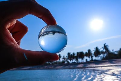 Close-up of hand holding crystal ball against blue sky