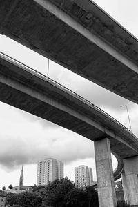 Low angle view of elevated road amidst buildings against sky