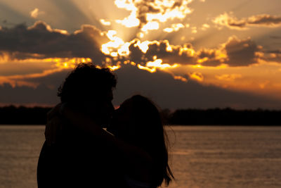 Silhouette couple kissing against sea at sunset