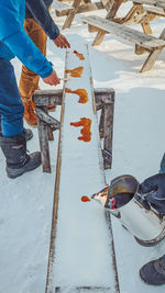 Low section of men pouring liquid on snow covered bench