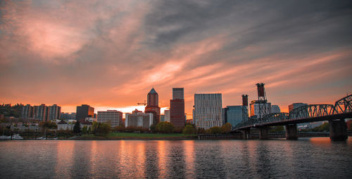 River by buildings against sky during sunset