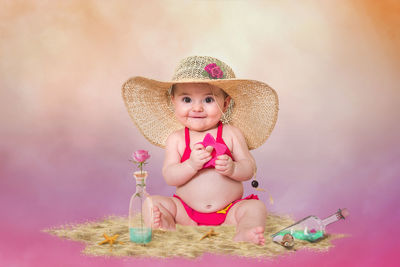 Portrait of cute baby girl in hat sitting against colored background
