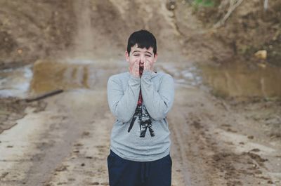 Boy shouting while standing on muddy field
