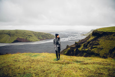 Woman standing on mountain against cloudy sky