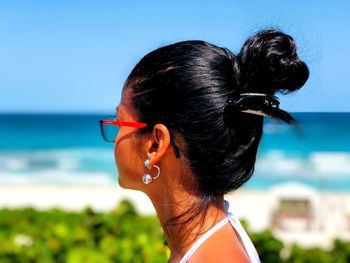 Side view of woman wearing sunglasses at beach against clear blue sky