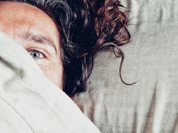 High angle portrait of woman hiding face with blanket while lying on bed at home