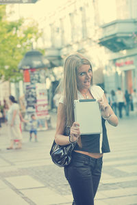 Portrait of young woman holding digital tablet while walking on city street