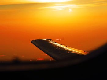Close-up of airplane wing against orange sky