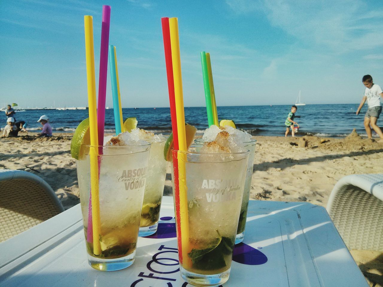 sea, drink, beach, horizon over water, food and drink, refreshment, sky, table, water, sand, shore, drinking glass, drinking straw, summer, vacations, freshness, incidental people, cloud - sky, outdoors, restaurant