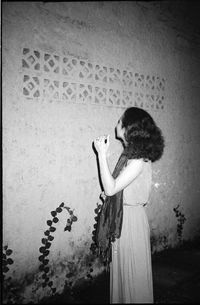 Young woman holding umbrella standing against wall