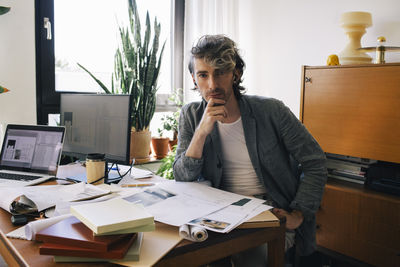 Portrait of male architect sitting with hand on chin at desk in home office