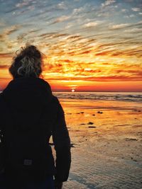 Rear view of woman looking at sea against sunset sky