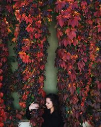 Young woman holding ivy against wall