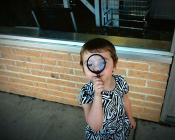 Portrait of cute girl looking through magnifying glass on sidewalk