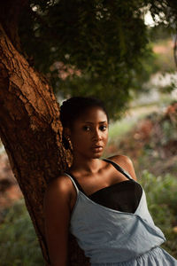 Young woman looking away while sitting on tree trunk in forest