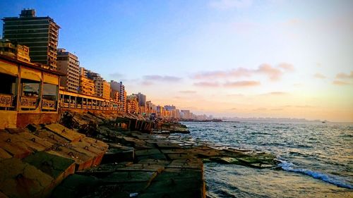 Buildings by sea against sky during sunset