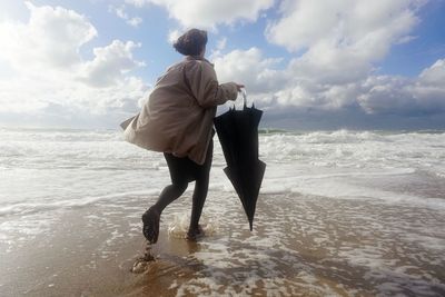 Rear view of woman walking on shore against sky