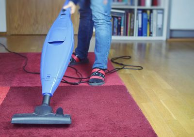 Low section of person cleaning floor with at vacuum cleaner at home