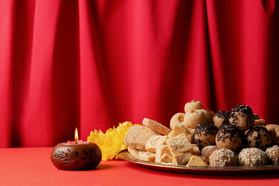 Indian traditional sweets laddu, soan papdi, burfi for festival on red background with with candles