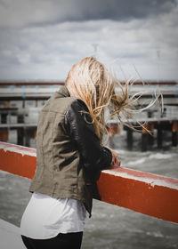 Rear view of woman standing on shore against sky