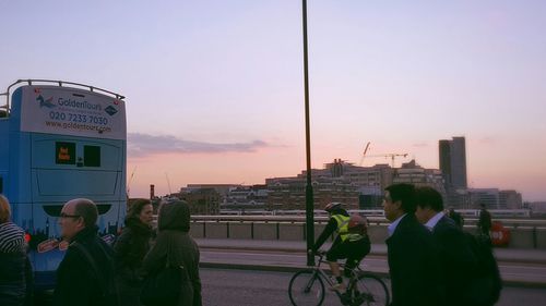 People standing on street in city against sky during sunset