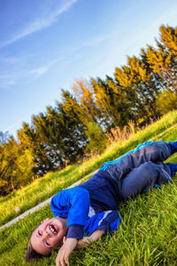 Portrait of smiling woman lying on grass against blue sky