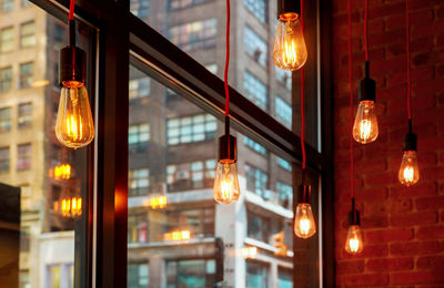 Low angle view of illuminated light bulbs hanging at ceiling by window