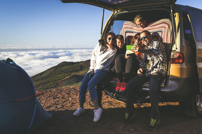 Family taking selfie while sitting in caravan against sky