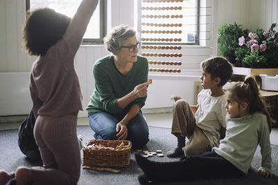 Senior female teacher playing puzzle game with preschool children while sitting in classroom at kindergarten