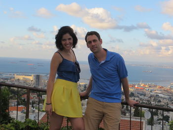 Portrait of smiling friends standing by railing in city against sky