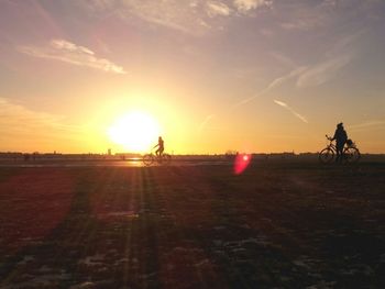 People riding bicycle on land against sky during sunset